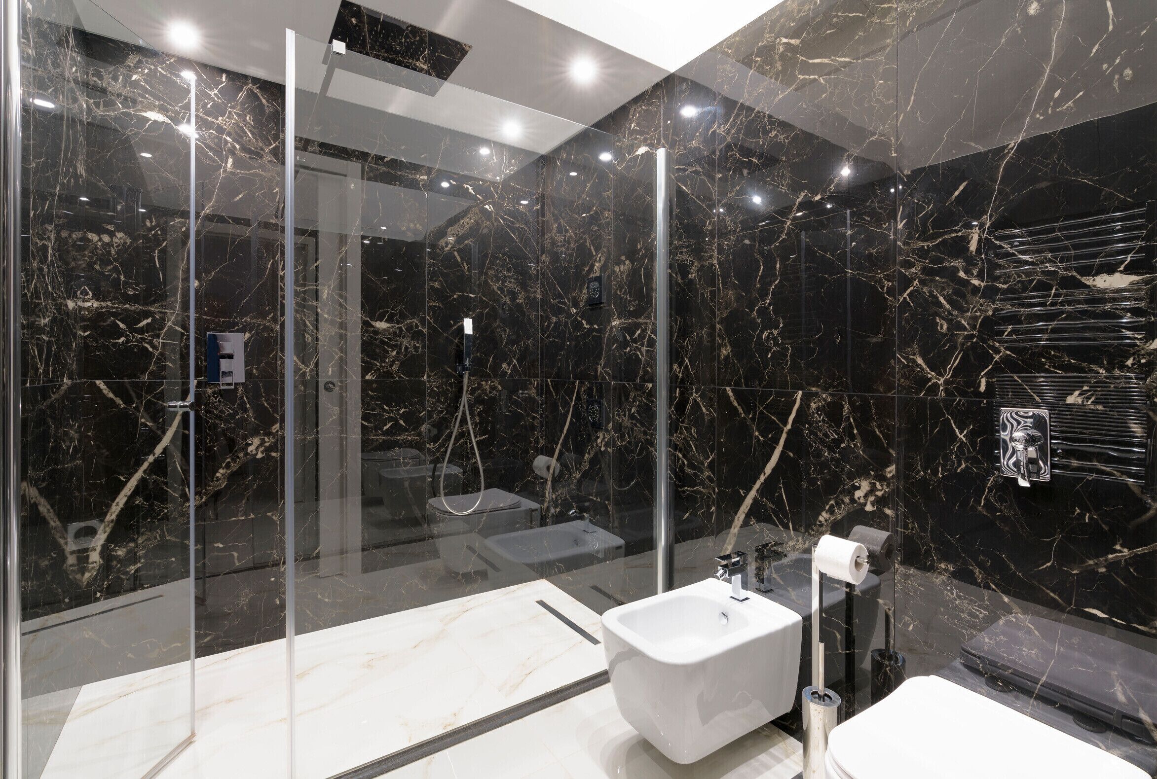 Ein modernes Badezimmer mit einer Glaskabine zur Dusche, einem weißen Waschbecken und Marmorwänden.
