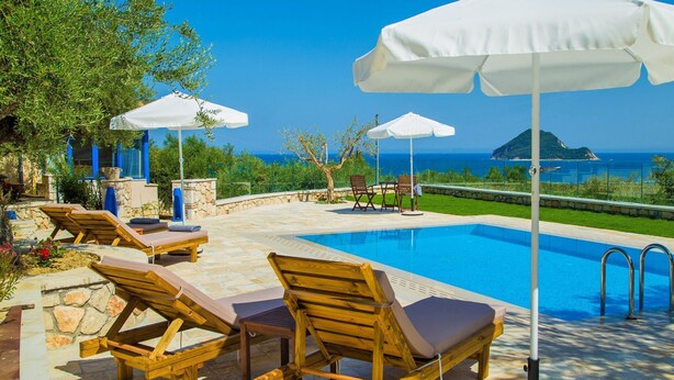 A poolside area with lounge chairs and umbrellas, a clear view of the sea, and a stone pathway. - 3 Bedroom Villa, Agios Sostis, Zakynthos (Lithakia)