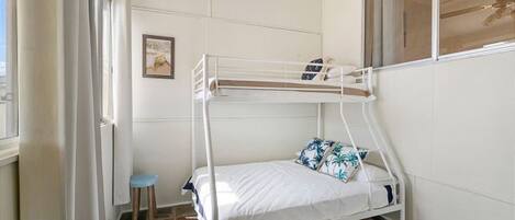 A bunk bed with a small stool, a framed picture on the wall, and a window with curtains.