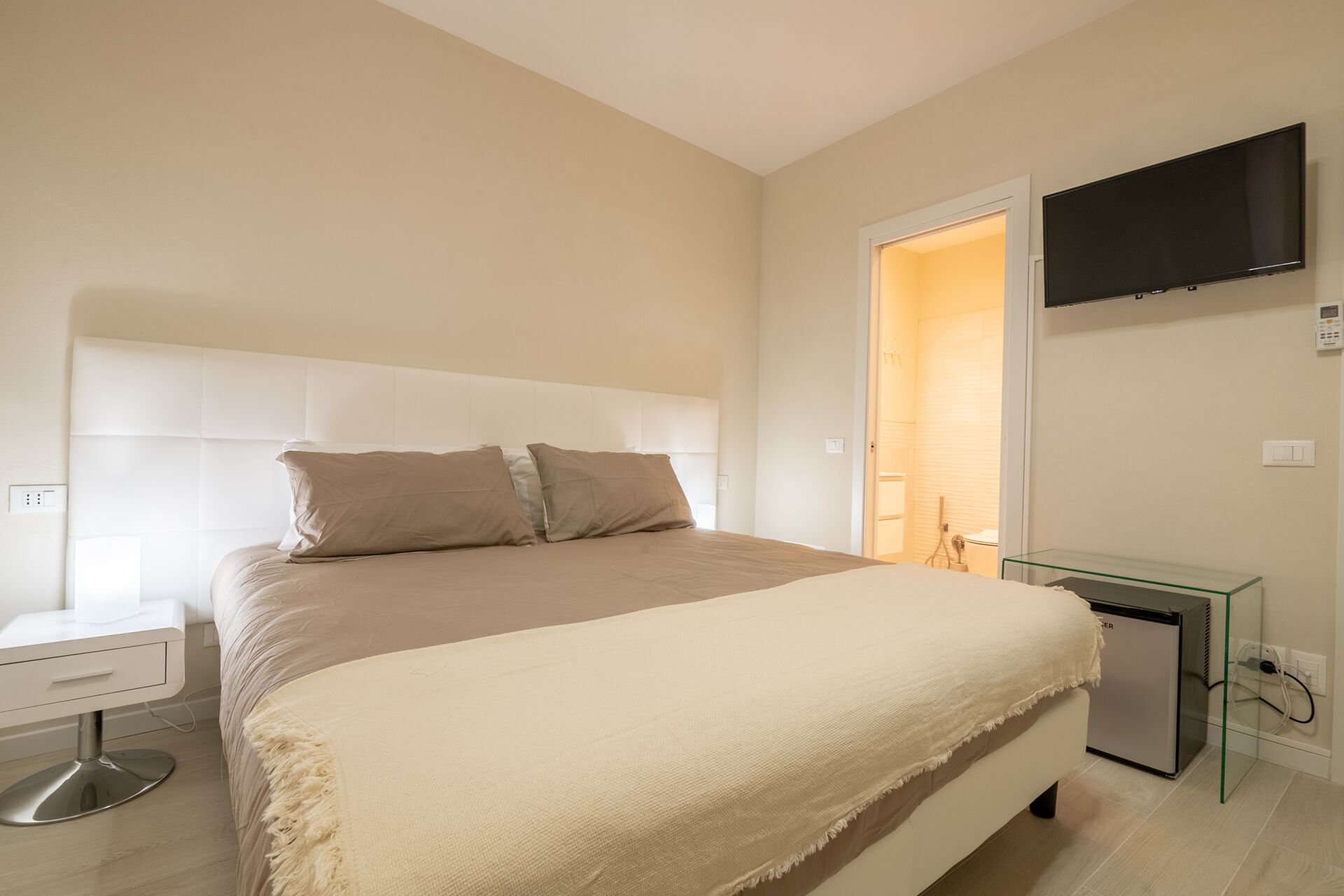 Un dormitorio con cama, mesita de noche y televisión montada en la pared.