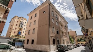 Ein mehrstöckiges Wohngebäude mit sandfarbener Fassade, mehreren Balkonen und einem Parkplatz mit einigen Autos.