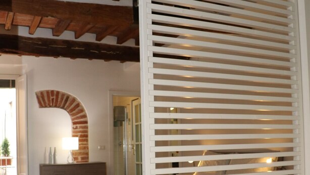A bedroom with a bed, a dresser, a lamp, and a white partition with horizontal slats.