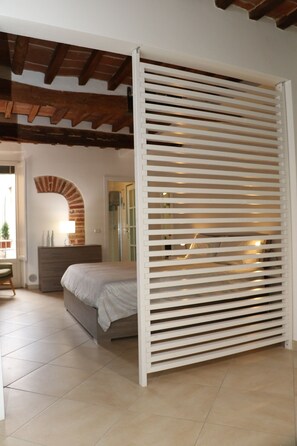 Een slaapkamer met een bed, een dressoir, een lamp en een witte wand met horizontale latten.