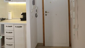 A small, well-lit kitchen with white cabinets, a wooden ceiling, and a white door.