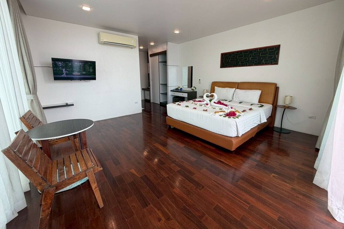 Una habitación de hotel con suelo de madera, una cama con ropa blanca, un televisor en la pared y una pequeña mesa con sillas.