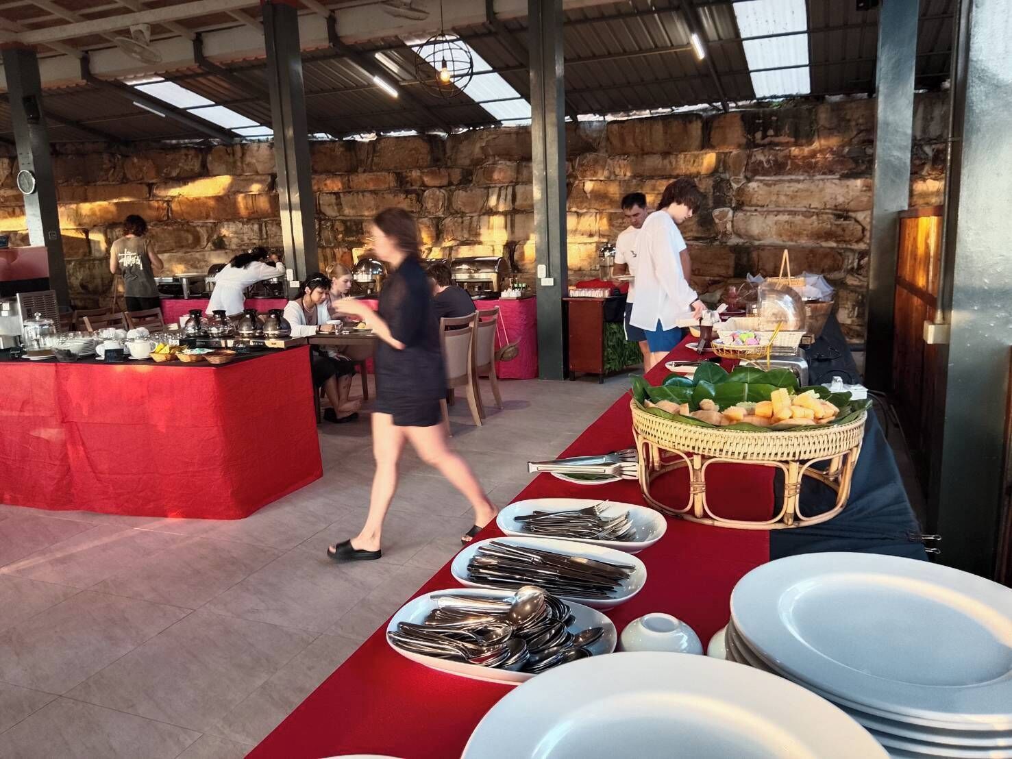 A buffet setup with a red tablecloth, plates, cutlery, and a wicker basket with food items.