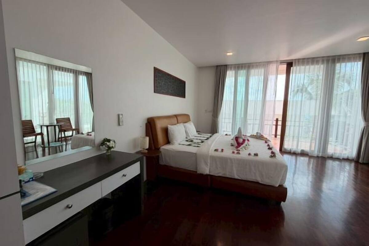 Un dormitorio con cama, escritorio, silla, un espejo grande y una ventana con cortinas.