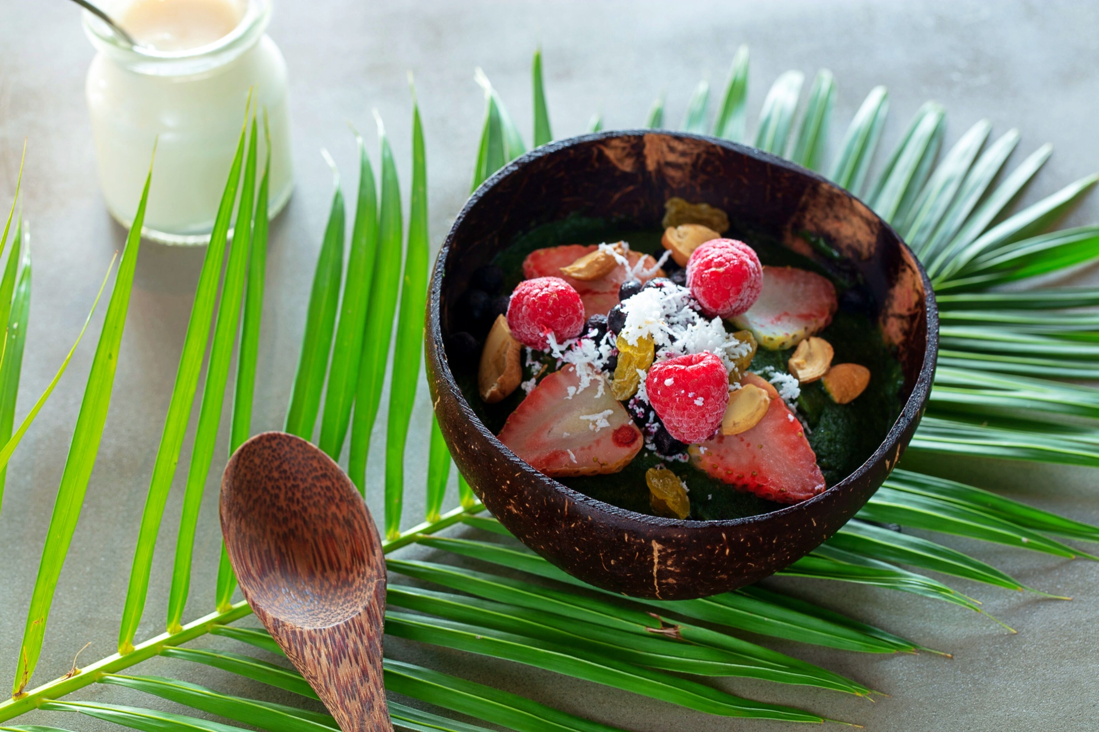 Uma tigela de sobremesa com frutas e nozes, acompanhada de uma colher de pau e um pote de creme.