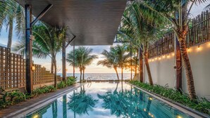 Ein Fernblick über den Ozean vom Infinity-Pool, umgeben von Palmen und einem überdachten Bereich mit Lichterketten.