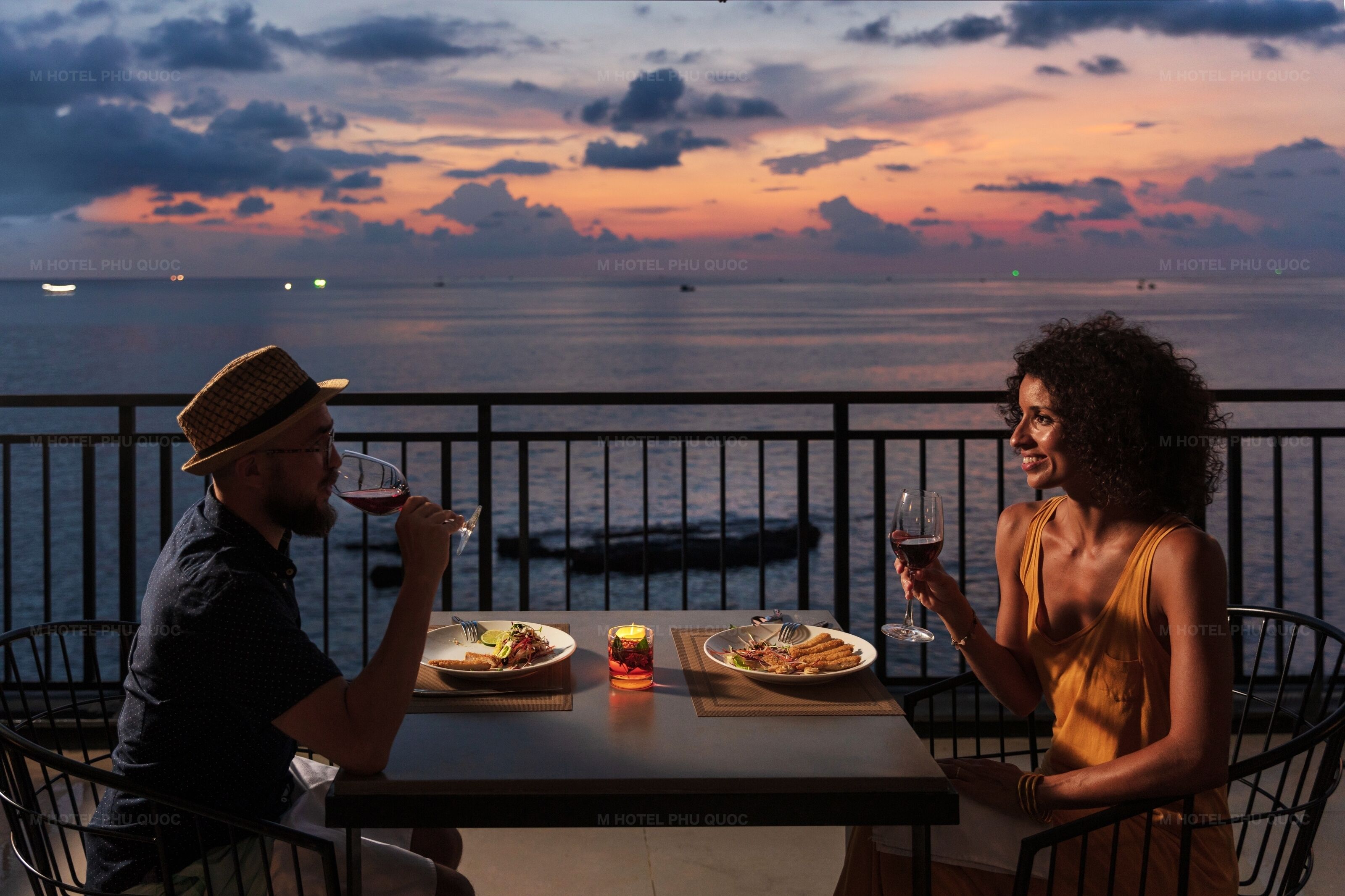 Two people dining at a table with a view of the sea and sunset.