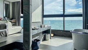 Ein modernes Hotelzimmer mit großem Fenster und Meerblick, einer Couch, einem Schminktisch mit Toilettenartikeln und einer Mülleimer.