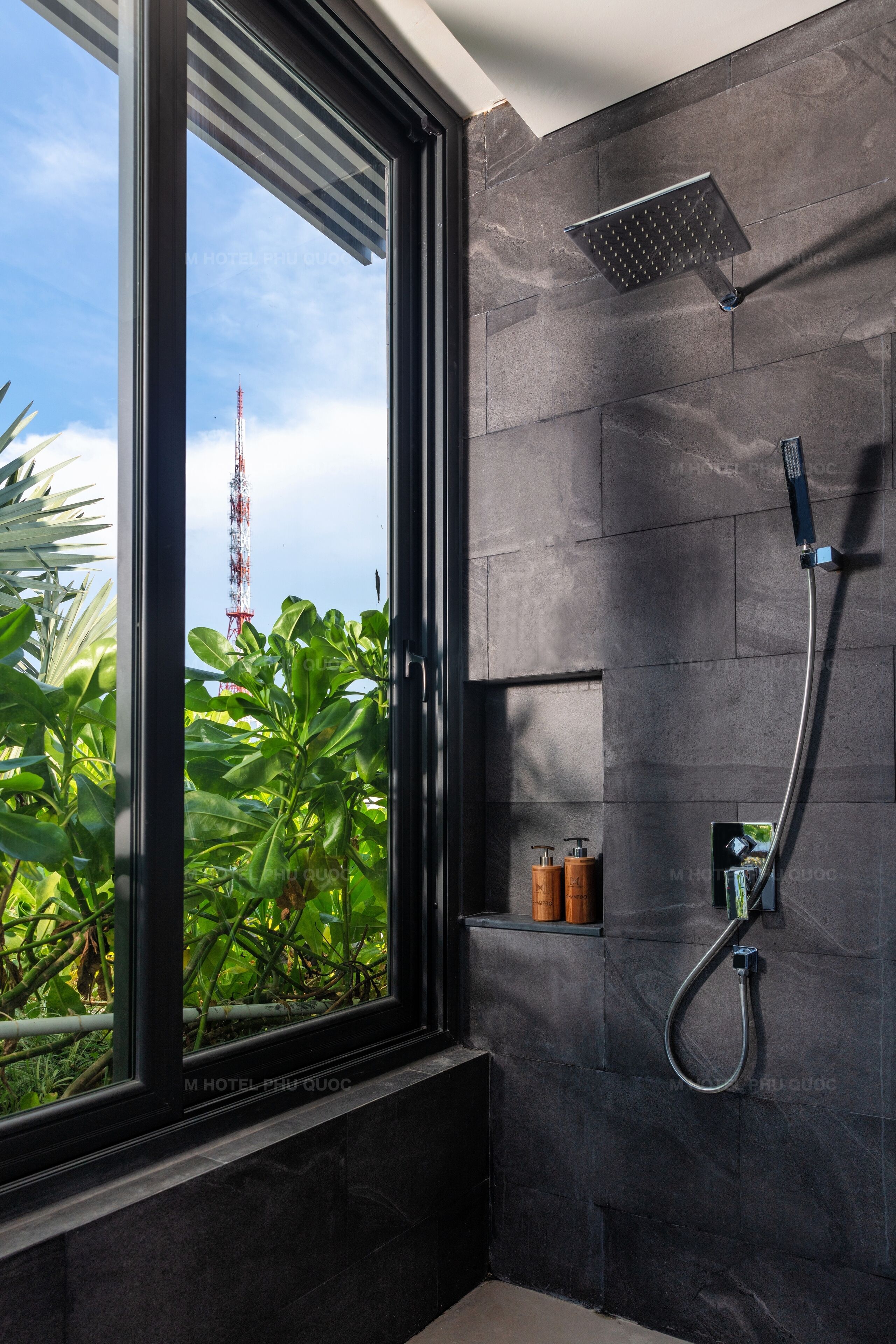 A modern bathroom with a large window, a shower, and a small shelf with toiletries.