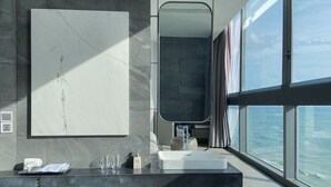Ein modernes Badezimmer mit einem großen Spiegel, einem Waschbecken und einem Fenster mit Blick auf den Ozean.