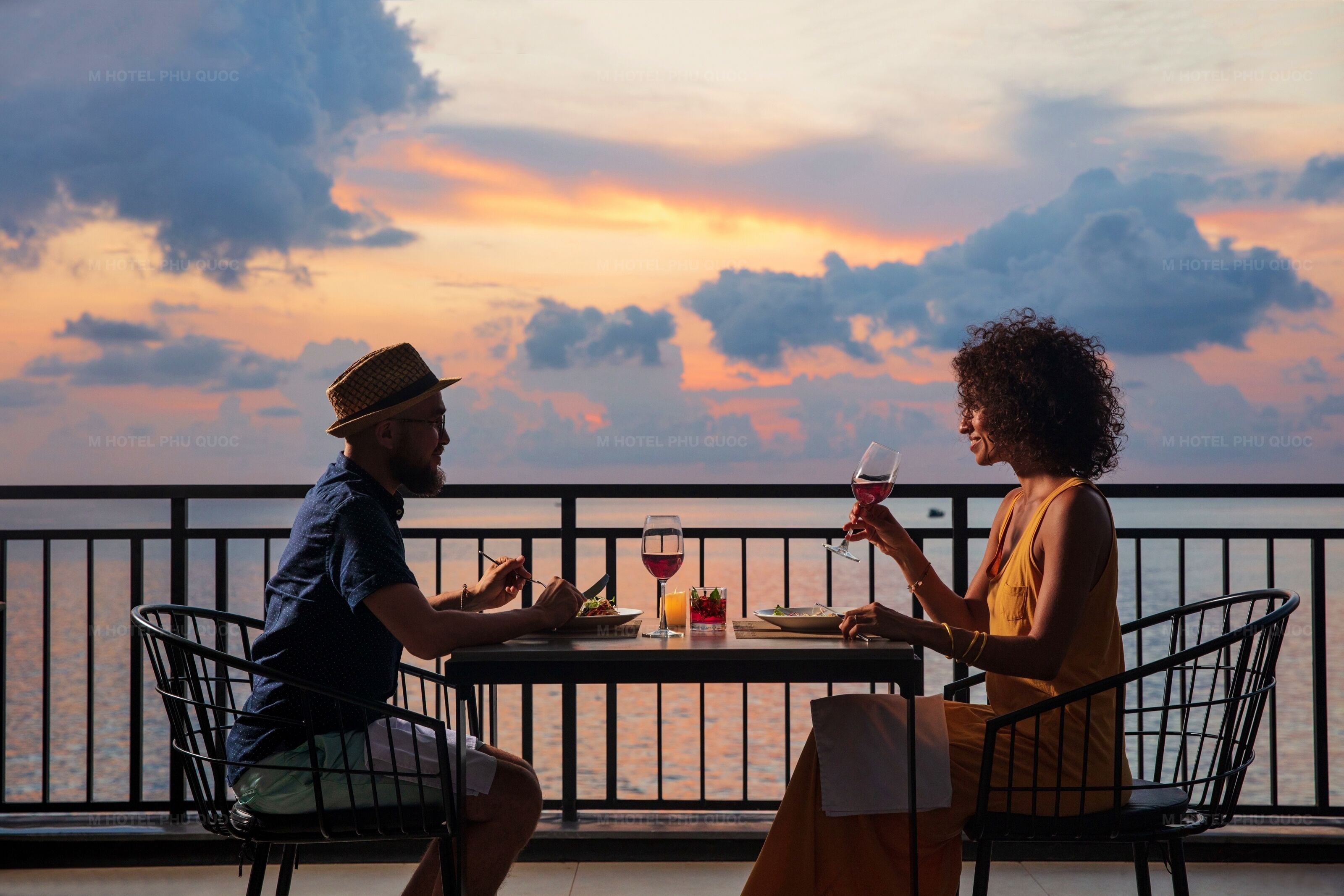 Two people dining at a table with a view of the sea and sunset.