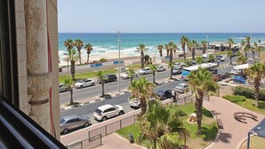 A coastal road with parked cars, palm trees, and a view of the beach and ocean. - GK Apartments - Ben Gurion 105 (Bat Yam)