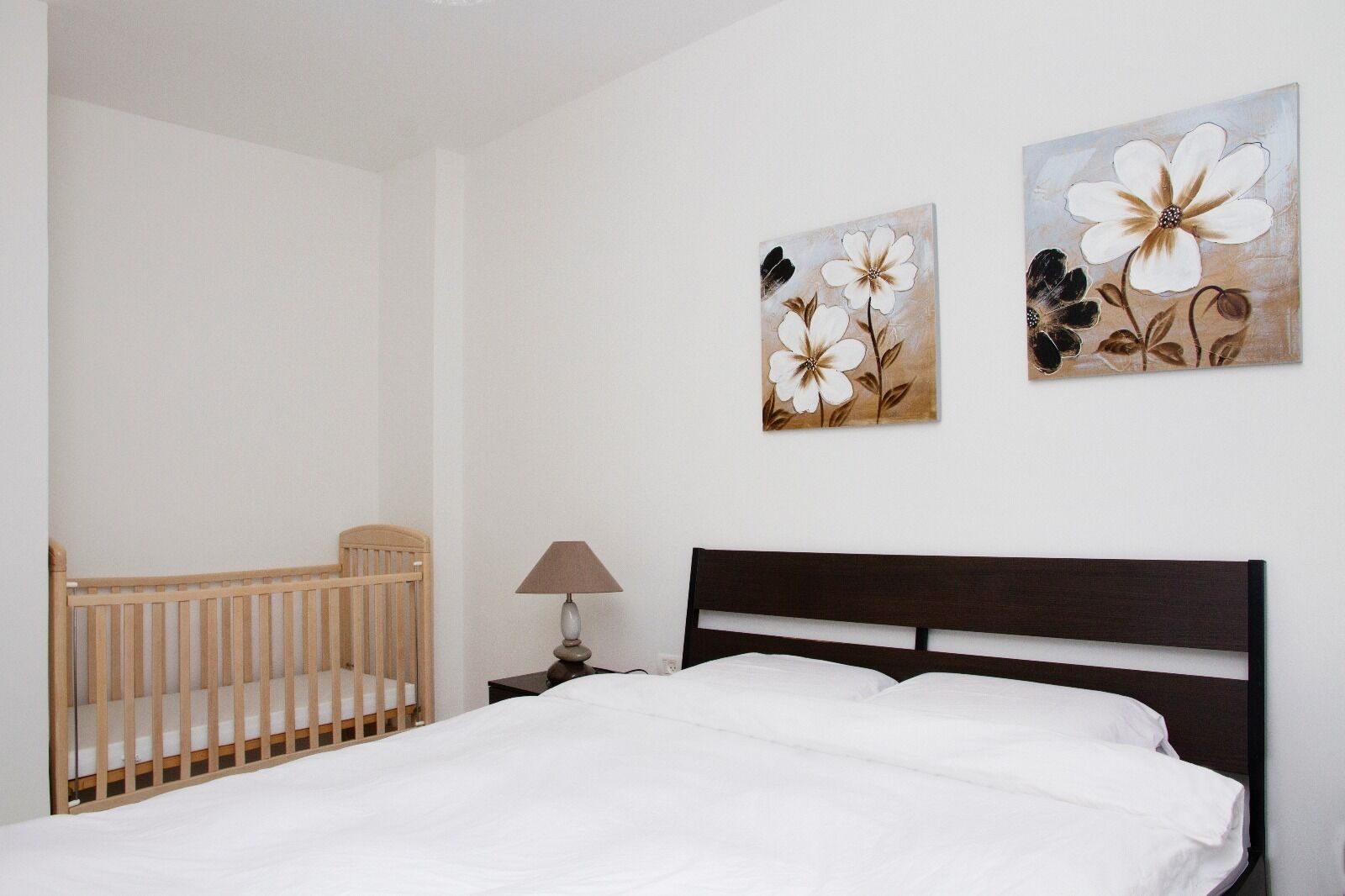 Una camera da letto con una culla, un letto e due quadri floreali appesi al muro.