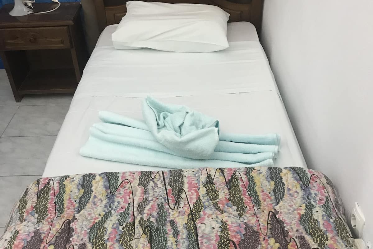 A neatly made bed with a patterned blanket, a white pillow, and a wooden headboard.