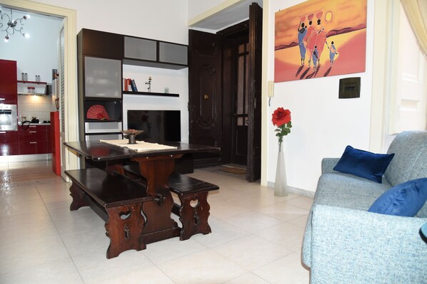 A modern living room with a dark wooden coffee table, a blue sofa with blue cushions, and a red decorative item on the wall. - Costigliola Baroque Palace APT next MANN (Napoli)