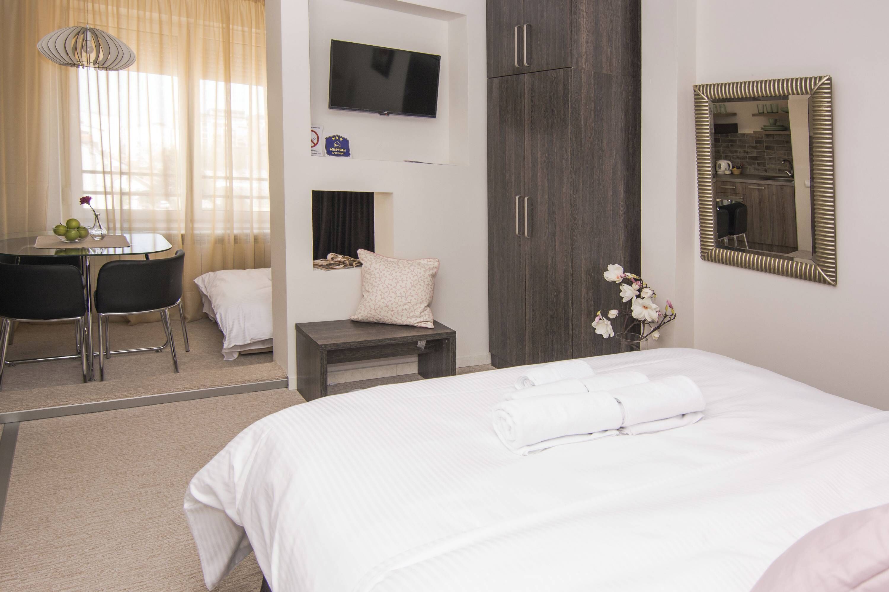 A hotel room with a bed, a desk with chairs, a television, a wardrobe, and a mirror.