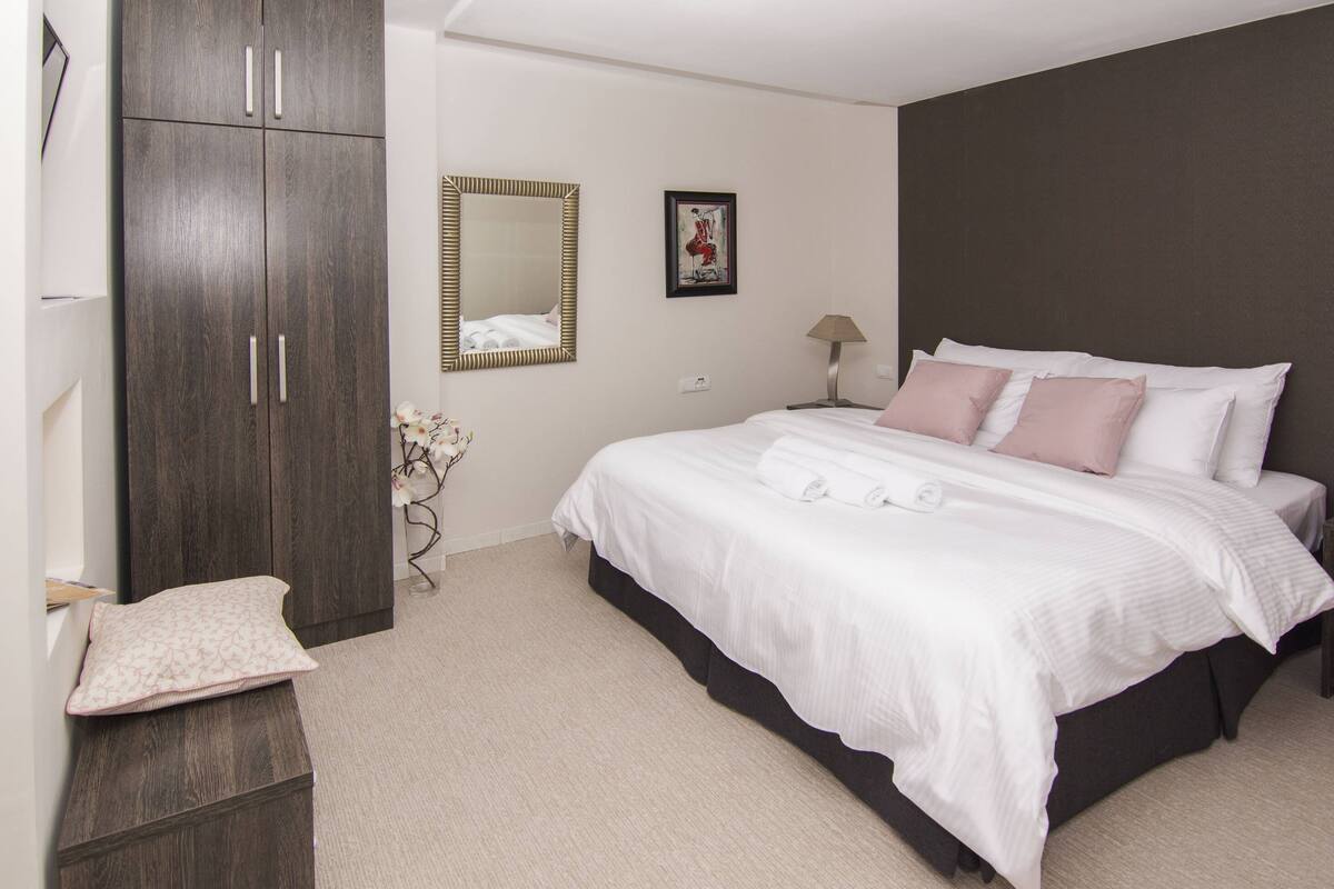 Une chambre à coucher avec un grand lit, une armoire, un miroir et une petite table avec une lampe.
