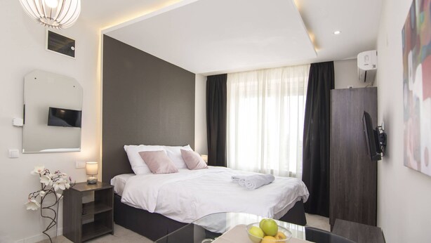 A modern hotel room with a large bed, bedside table, and a glass table with fruit. - Beo Green View (Belgrade)