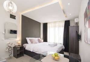 Una camera d'albergo moderna con un letto grande, un comodino e un tavolino in vetro con della frutta.