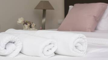 Una cama bien hecha con almohadas blancas y rosas, una toalla blanca enrollada y una lámpara al fondo.