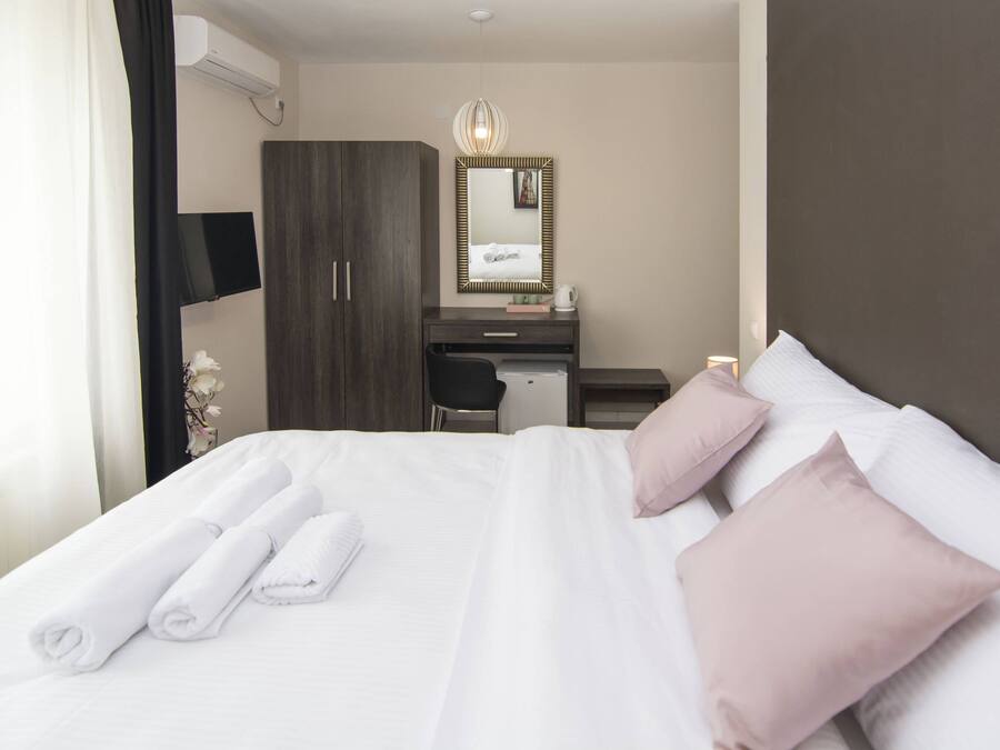 Quarto de hotel com cama, escrivaninha, cadeira, guarda-roupa e espelho.