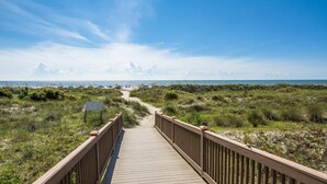 Un paseo marítimo de madera que lleva a una playa, con cielo despejado.