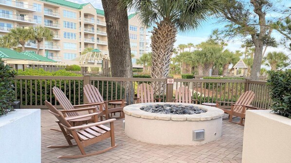Un patio con sillas Adirondack, un hogar a leña de piedra y vistas de un edificio de hotel con balcones.