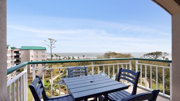 A balcony with a table and chairs, overlooking a beach and a residential area.