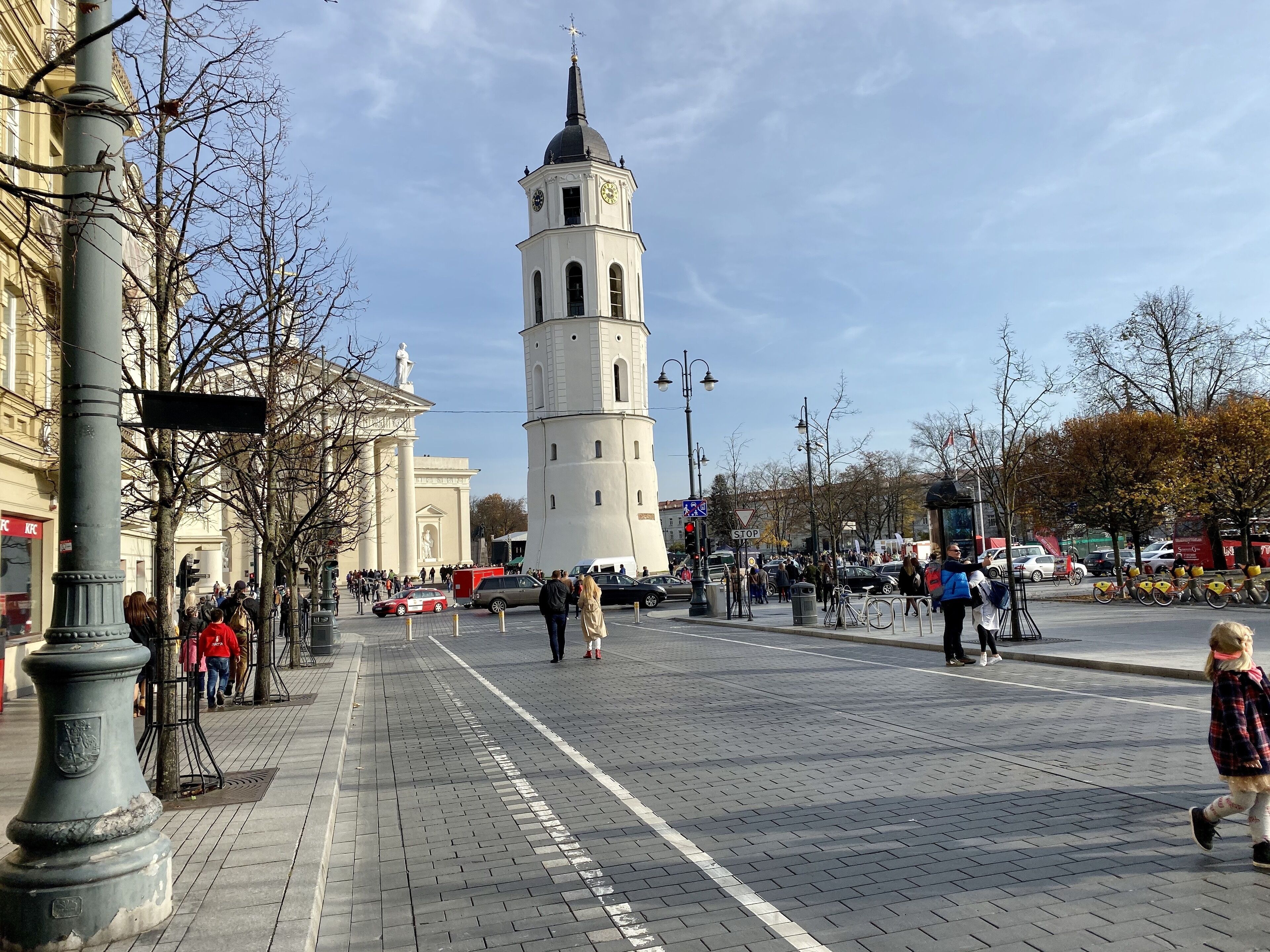 A historic tower with a clock, surrounded by a cobblestone plaza and modern buildings.