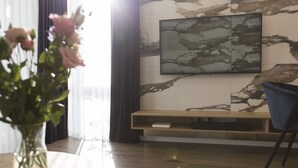 Ein modernes Wohnzimmer mit Marmorwand, einem Wand-Fernseher, einer Holzkonsole und einem Blumenstrauß.