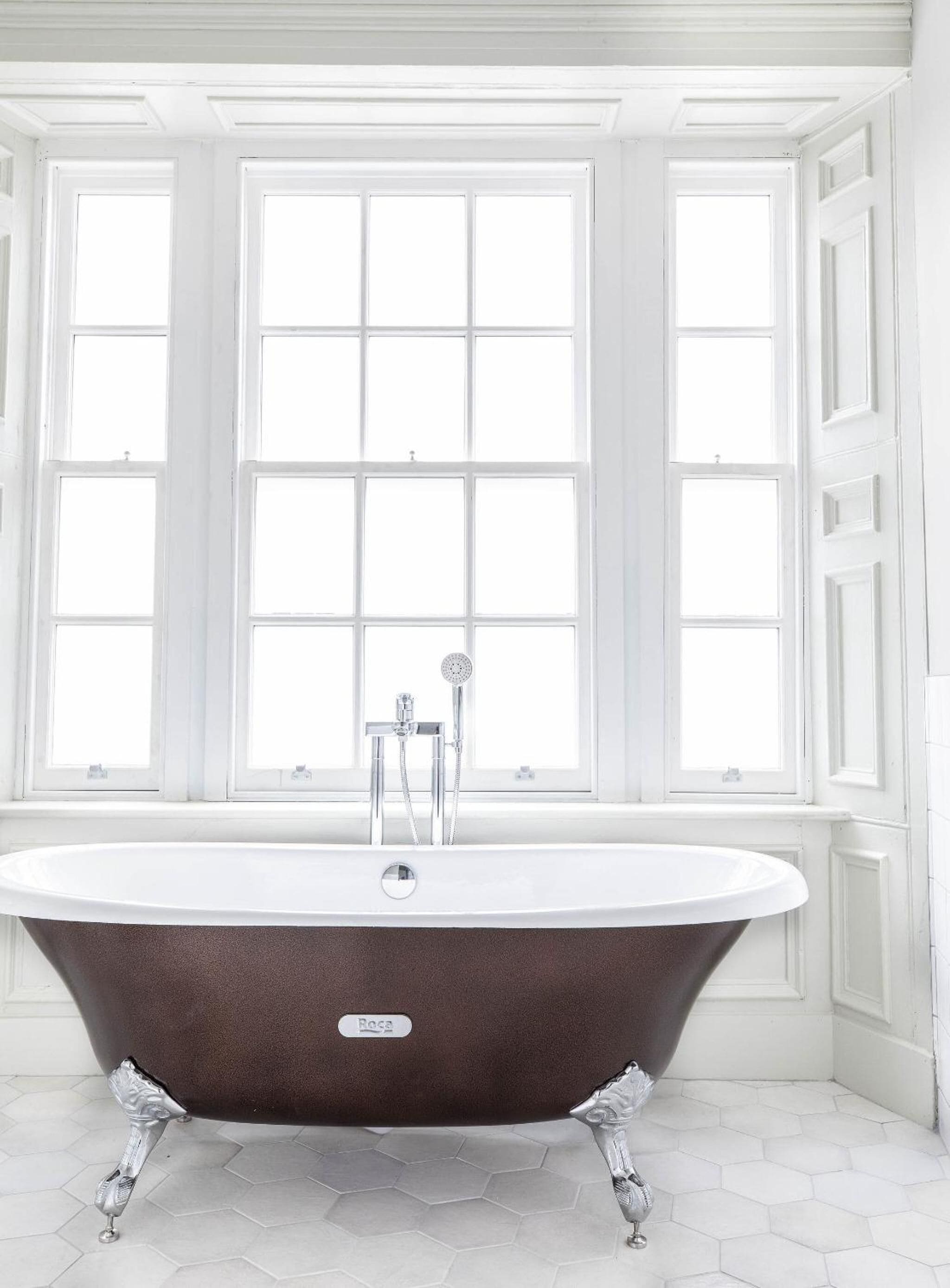 A clawfoot bathtub in a bathroom with large windows and white walls.