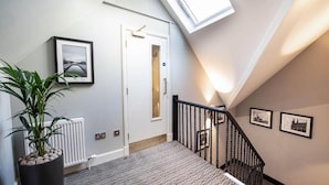 Un escalier avec une rampe noire, une plante en pot et des tableaux encadrés accrochés aux murs.
