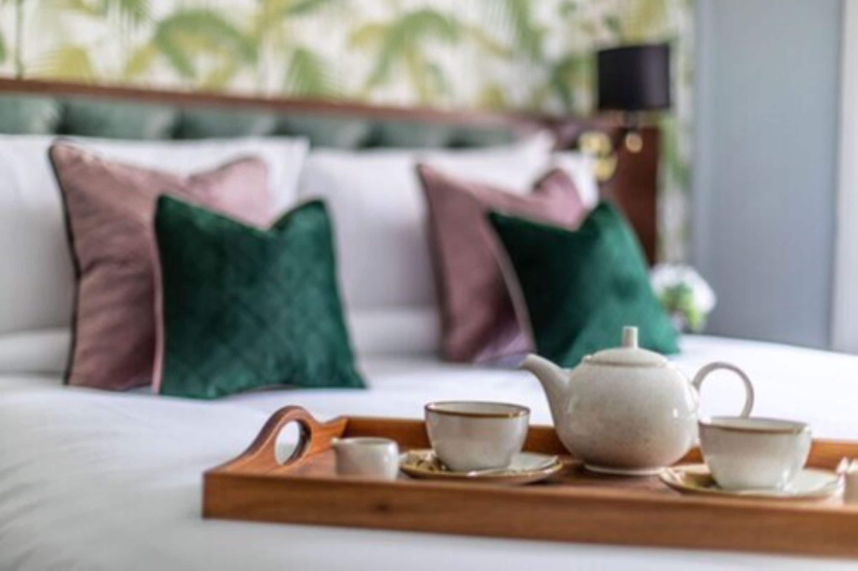 A neatly made bed with a tray of tea set and a teapot.