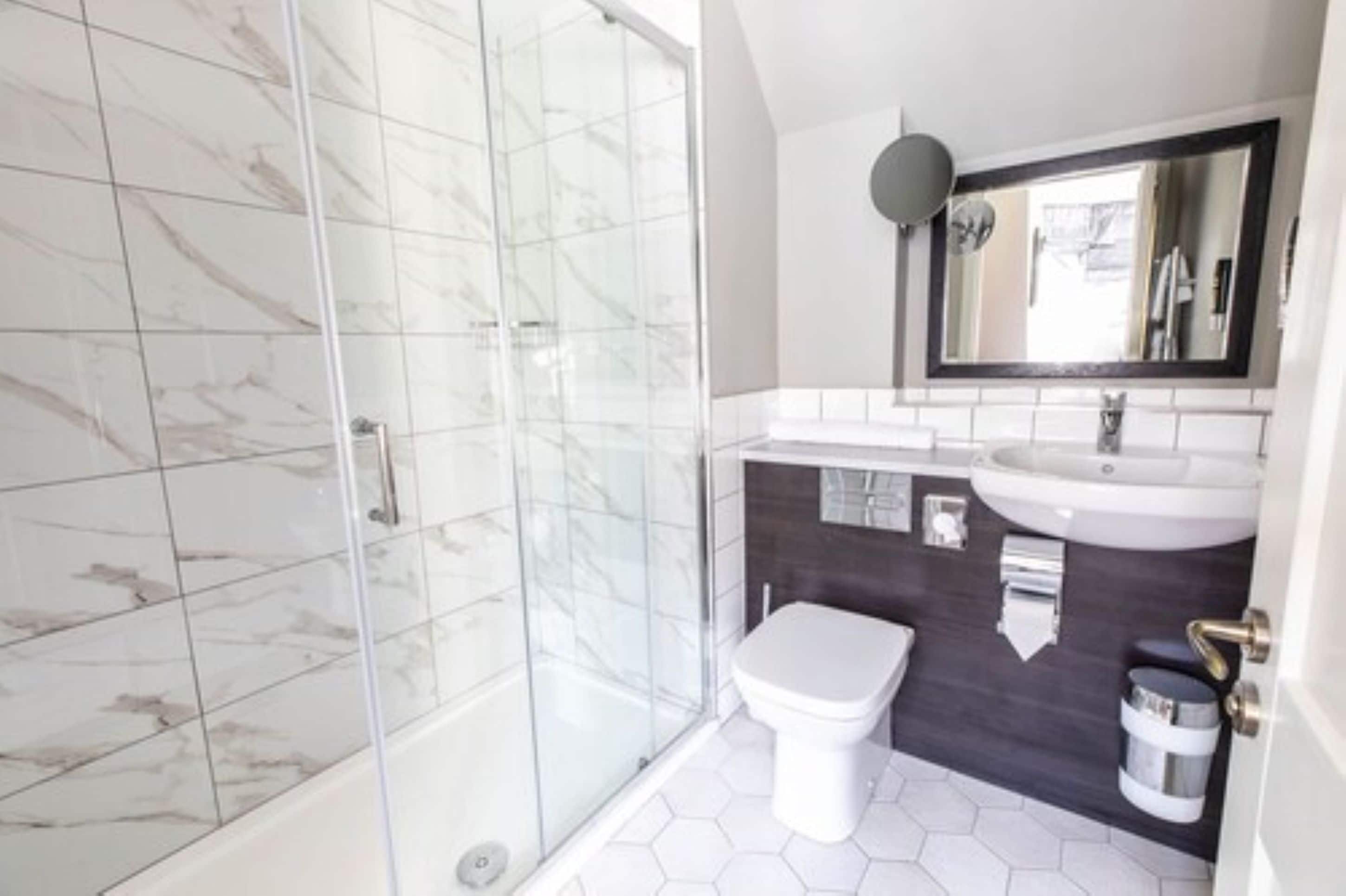 A modern bathroom with a glass shower enclosure, a white toilet, and a dark tiled backsplash.