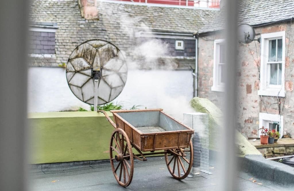 A rustic outdoor setting with a wooden cart and a large, circular, glass-like structure emitting steam.