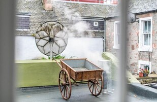 A rustic outdoor setting with a wooden cart and a large, circular, glass-like structure emitting steam.