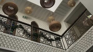 Interior espacioso con techos altos, tragaluces, lámparas colgantes de mimbre y barandillas de metal ornamentadas.