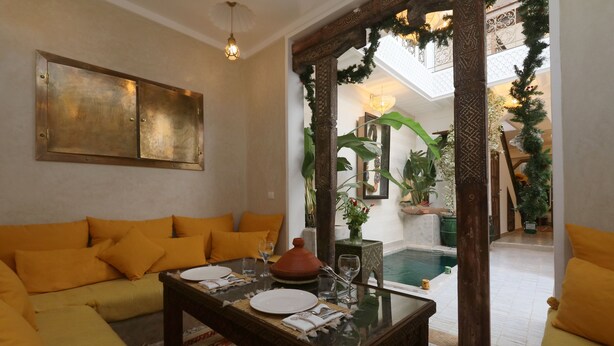 Un espacio de sala acogedor con un sofá, una mesa de centro de vidrio y una mesa de comedor para dos. Se ve una piscina al fondo, lo que sugiere un ambiente relajante.