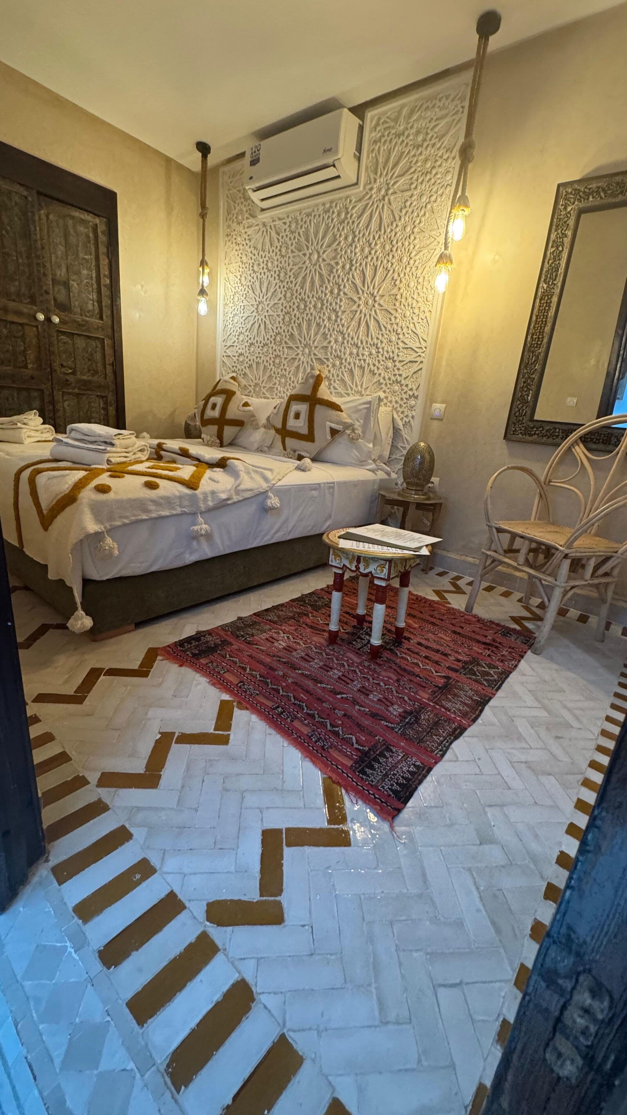 Un dormitorio con cama, mesita de noche, silla, alfombra estampada y decoración en la pared.