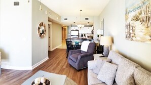 A modern living room with a flat-screen TV, a sofa, a coffee table, and a dining area in the background.