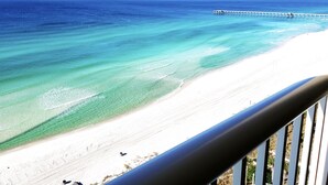 A beach with clear turquoise water, a white sandy shore, and a pier extending into the ocean.