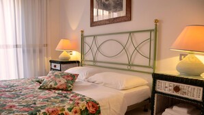 Cama bem arrumada com roupa de cama florida, duas luminárias de cabeceira e uma mesa de cabeceira de vime com toalhas.