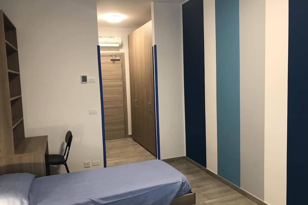 A bedroom with a bed, a desk, and a wardrobe.