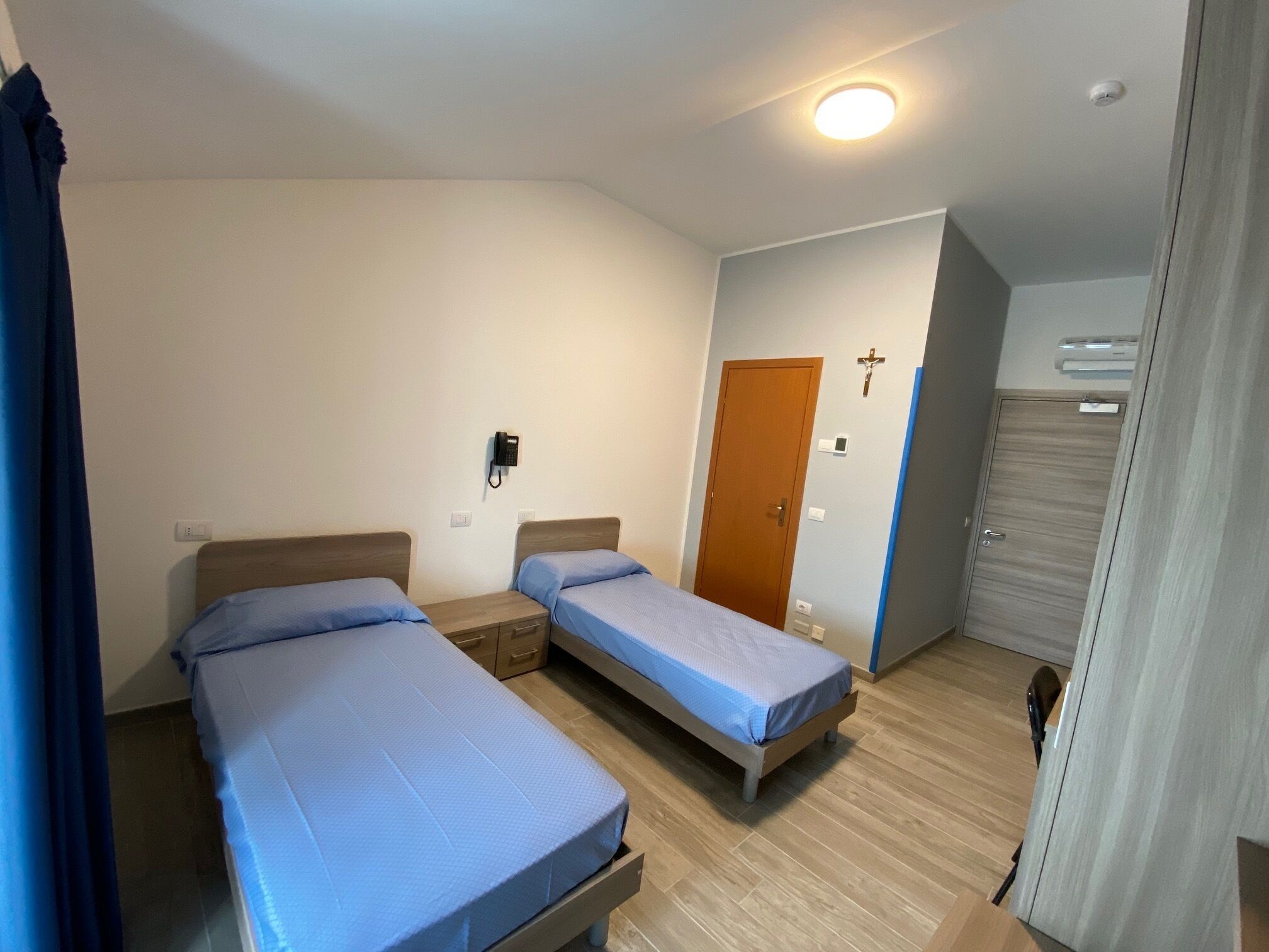 Et værelse med to senge, en trædør, et vægmonteret telefonapparat og en loftlampe.