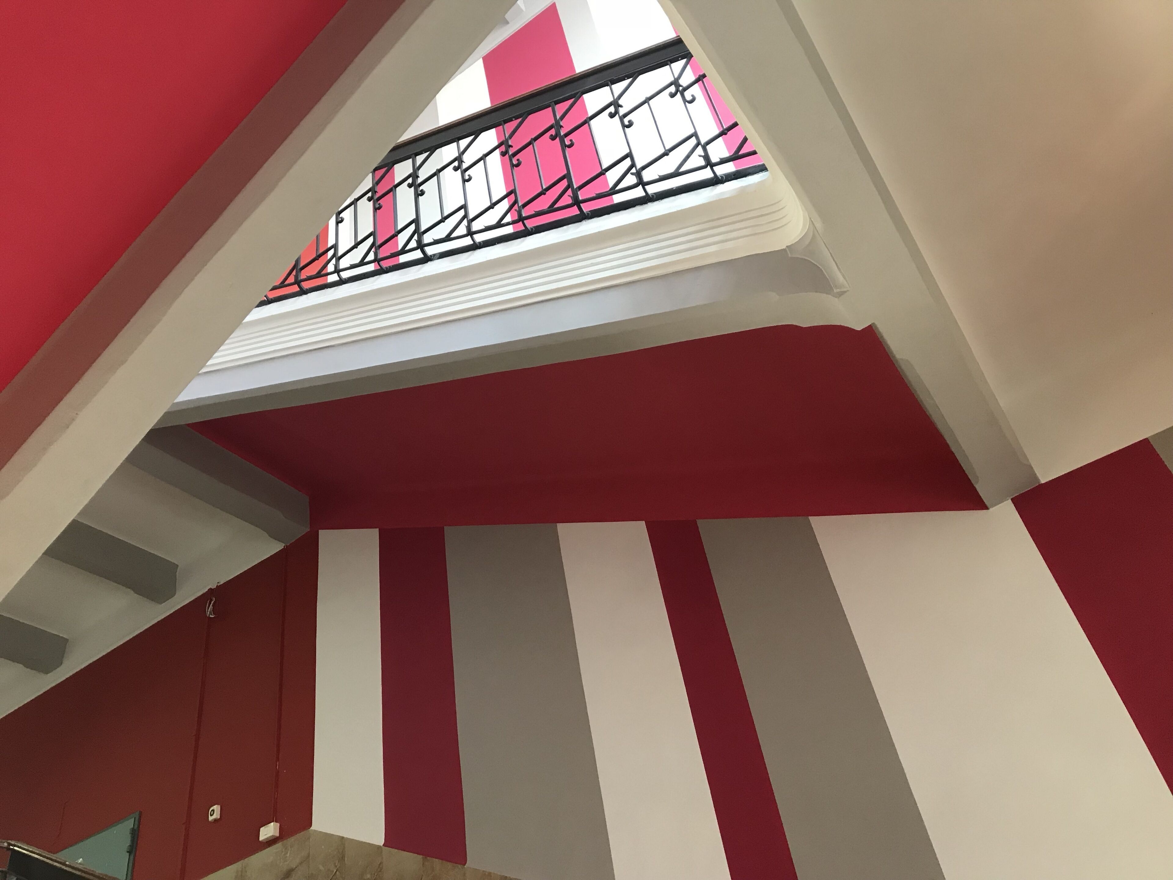 Una scala con un muro a righe rosse e bianche, una ringhiera in metallo e una finestra con motivo rosa e bianco.
