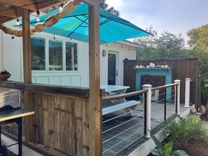 Una terraza de madera con mesa y sillas, una parrilla y una sombrilla azul que da sombra.