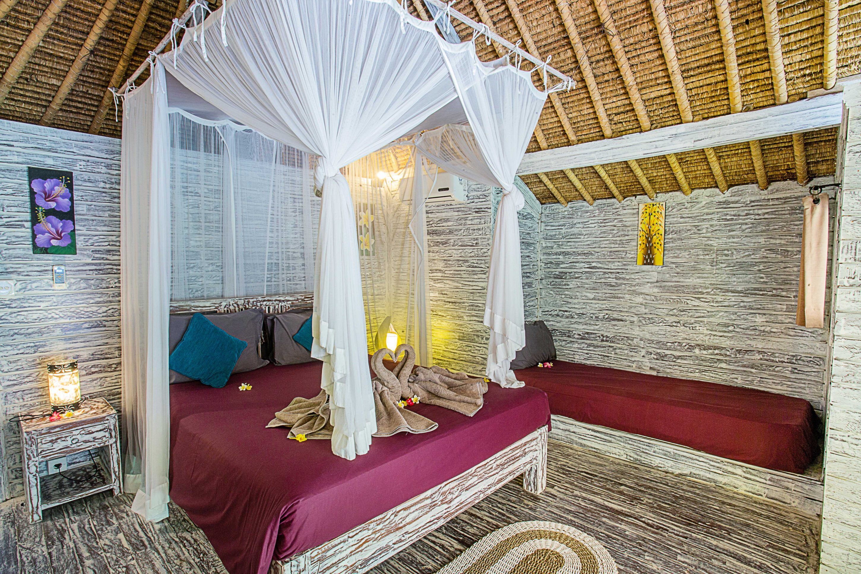 A room with a bed under a canopy, a nightstand with a lamp, and a stone-textured wall.